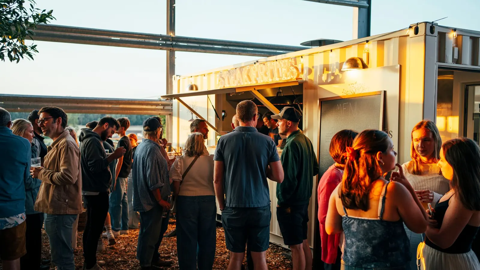 Guests gathered outside the lit container kitchen at Lopemede Farm on a summer evening
