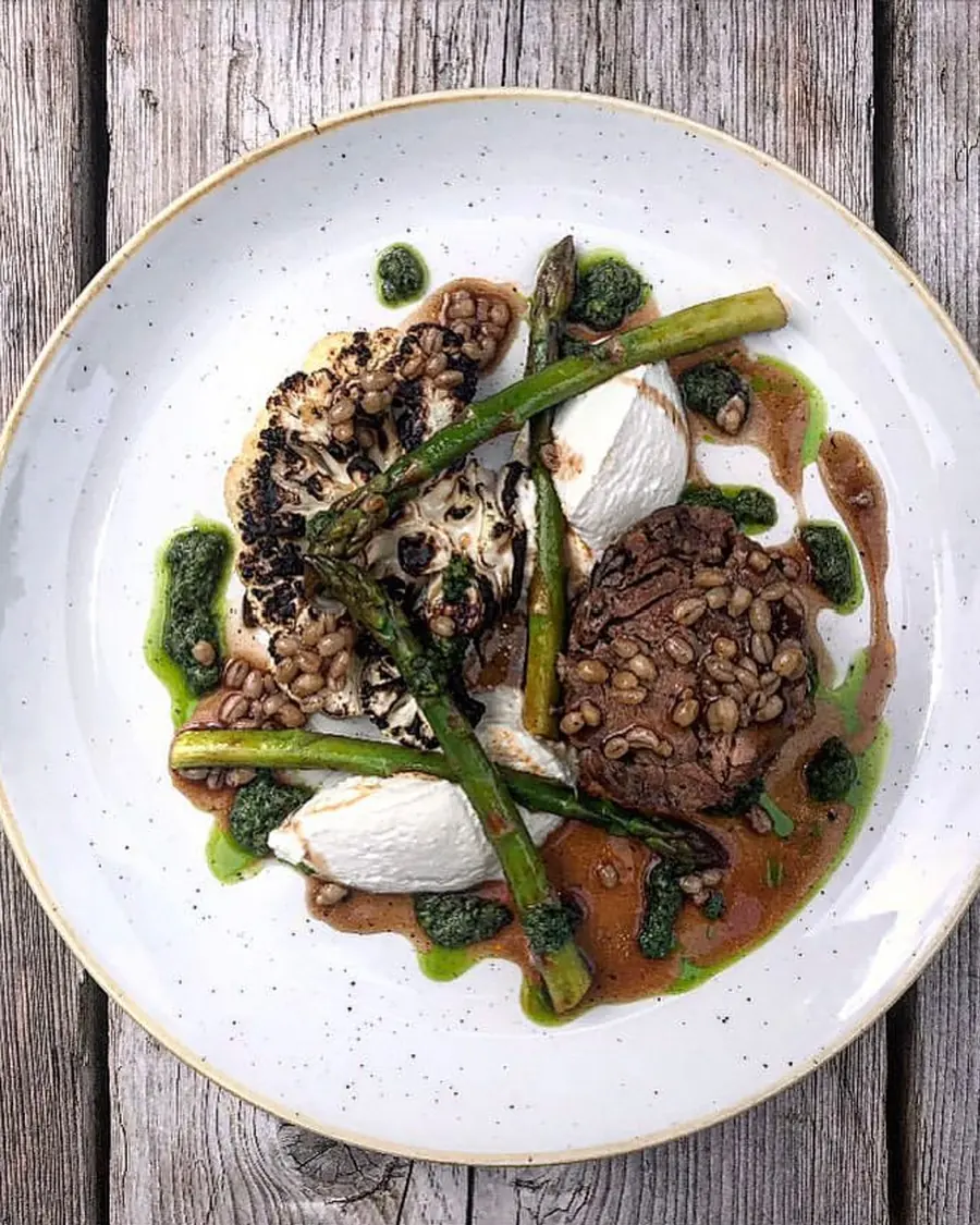 A plated seasonal dish with charred greens and salsa verde on a rustic table