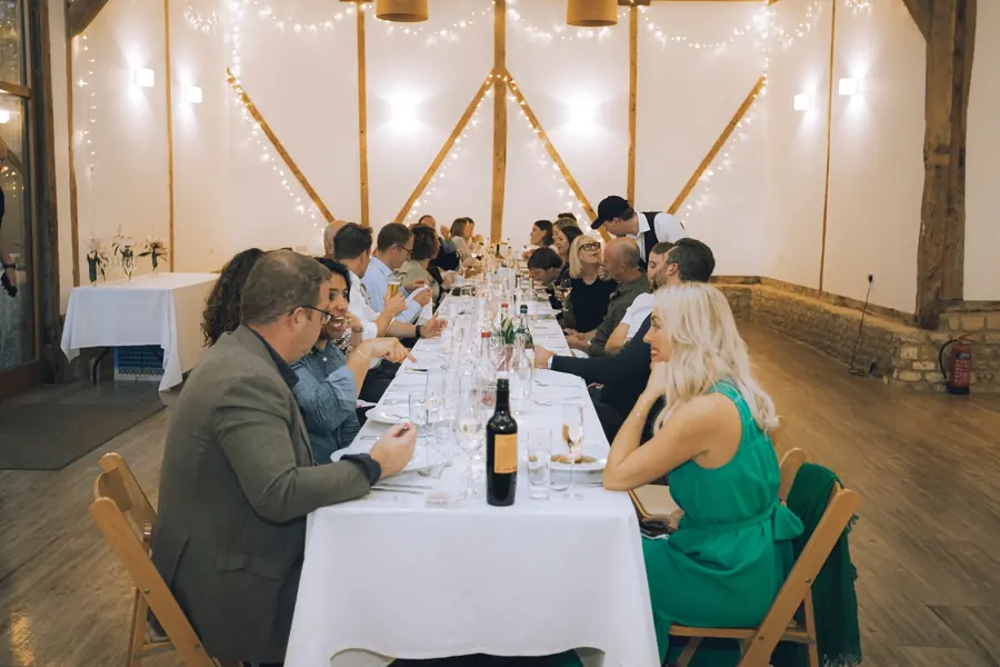 A long table of supper club guests dining under strings of lights in the barn